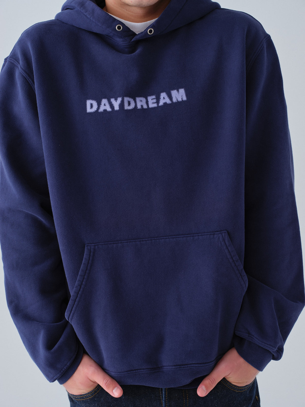 Person wearing a navy hoodie with 'DAYDREAM' text on a light gray background close up detail