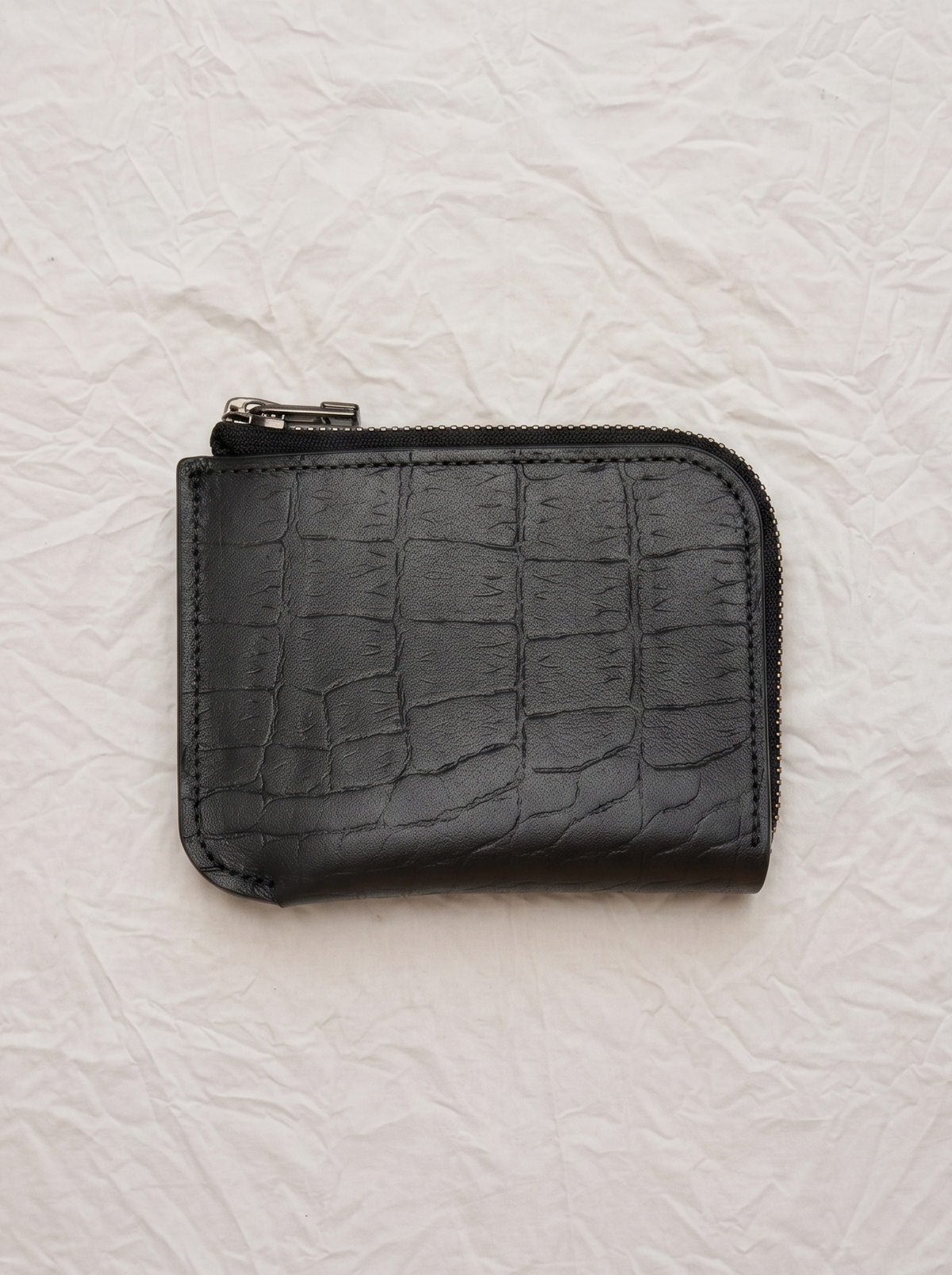 A small Hanover black zippered pouch with a crocodile-embossed texture, photographed flat on a wrinkled off-white paper background.