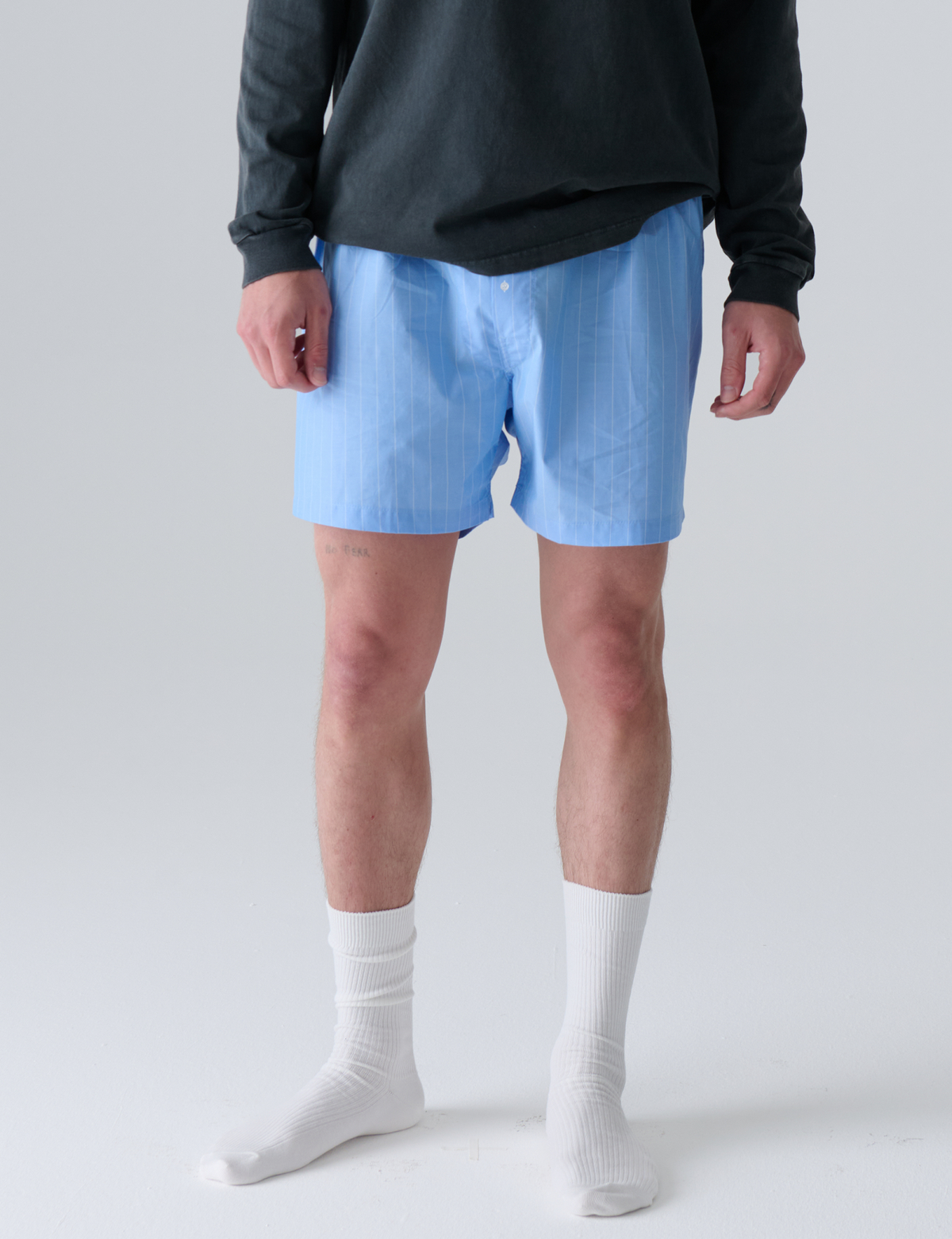 Person wearing light blue boxers and white socks on a plain background