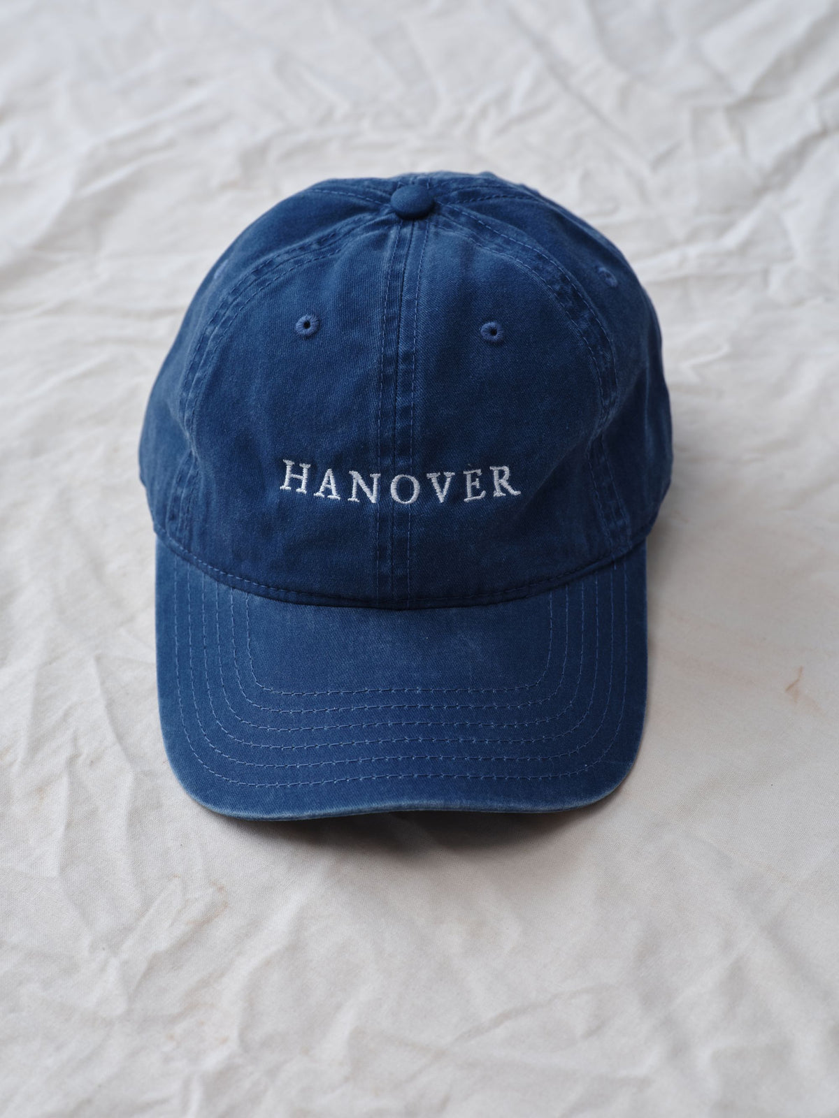 Navy blue cap with 'HANOVER' text on a textured white background