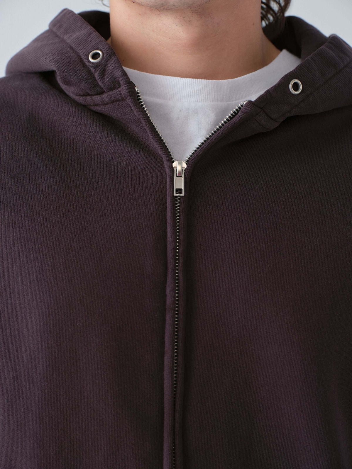 Close-up of a person wearing a  Hanover dark brown zip-up hoodie with a white shirt underneath.