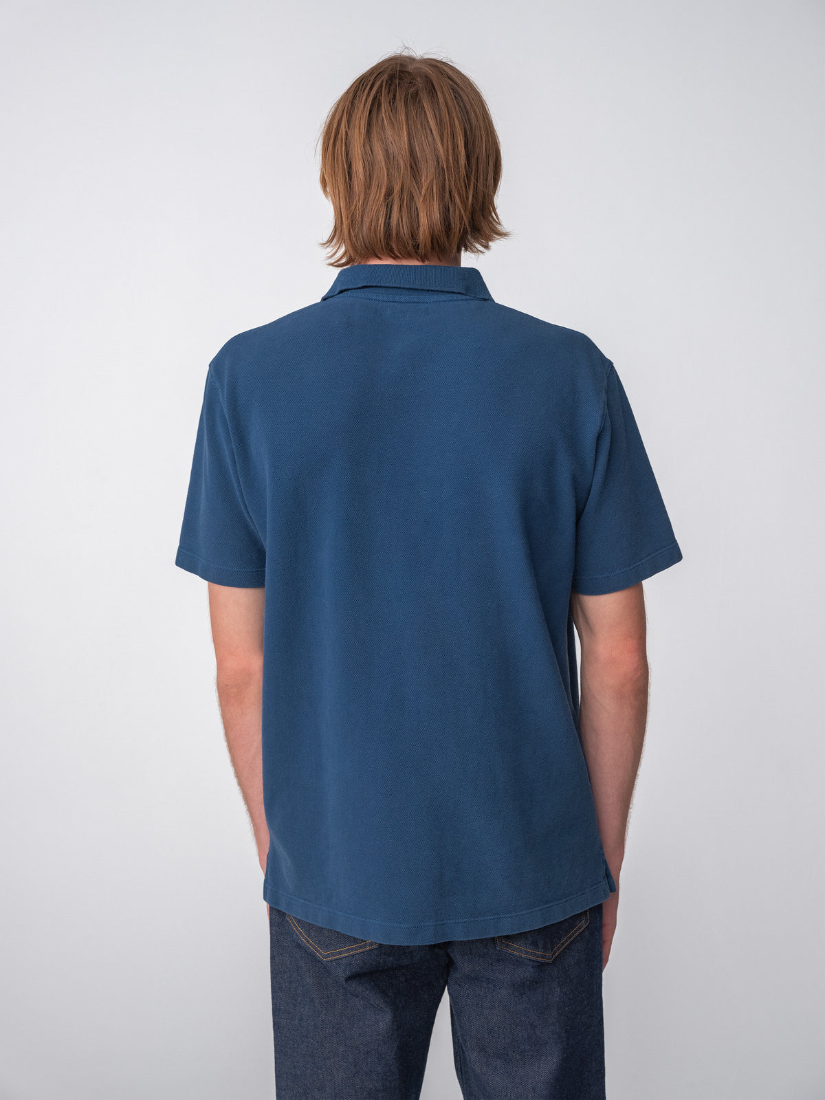Model wearing a Sunwashed Staple Polo Shirt in mid navy color, back view